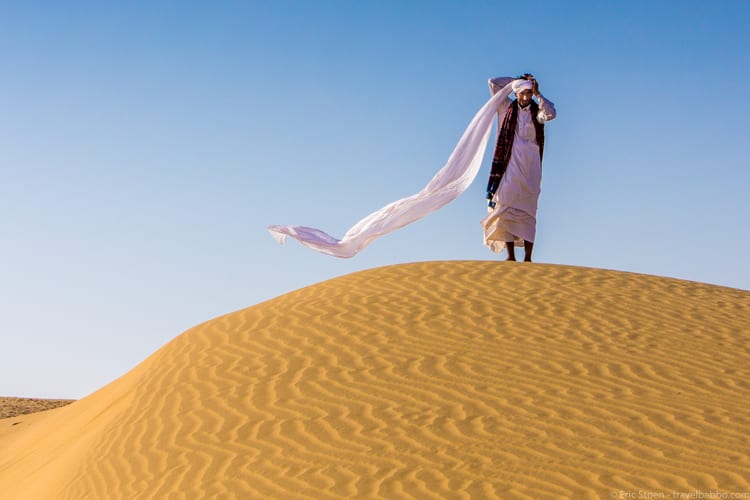 Travel Photography Tips - A perfect moment in Rajasthan, India. I asked my camel jockey to walk to the top of the dune, since I loved the late afternoon light and the leading lines. The turban coming undone was just luck. Shot in Program mode. 